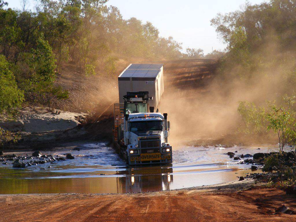 Northern Transportables prime mover hauling a transportable building through a water crossing on a dusty outback road