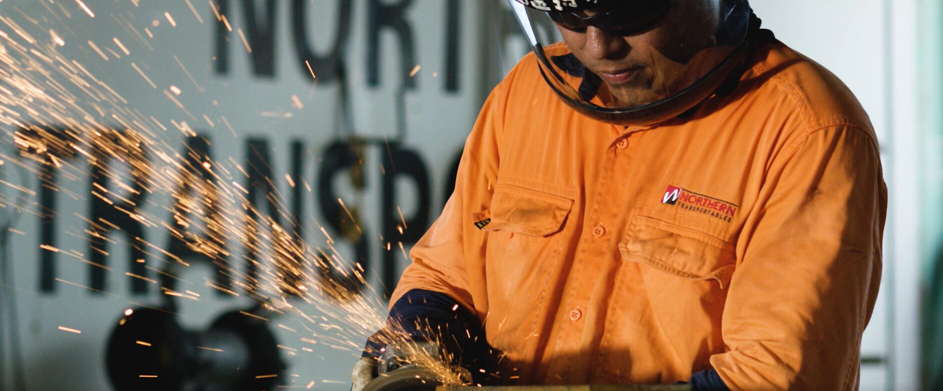 Northern Transportables tradesperson in a welding helmet grinding steel in the workshop, sparks flying